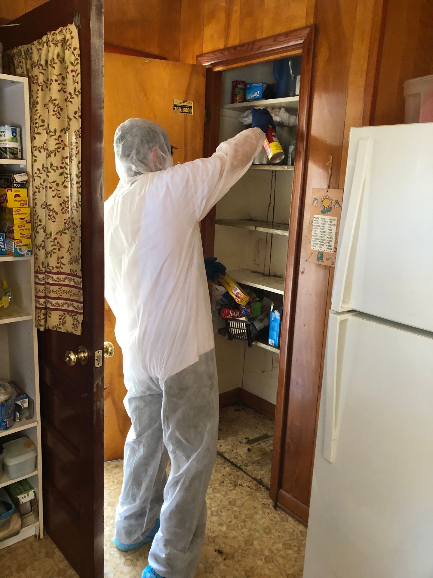 Person in protective clothing sprays inside a wooden cabinet in a kitchen.