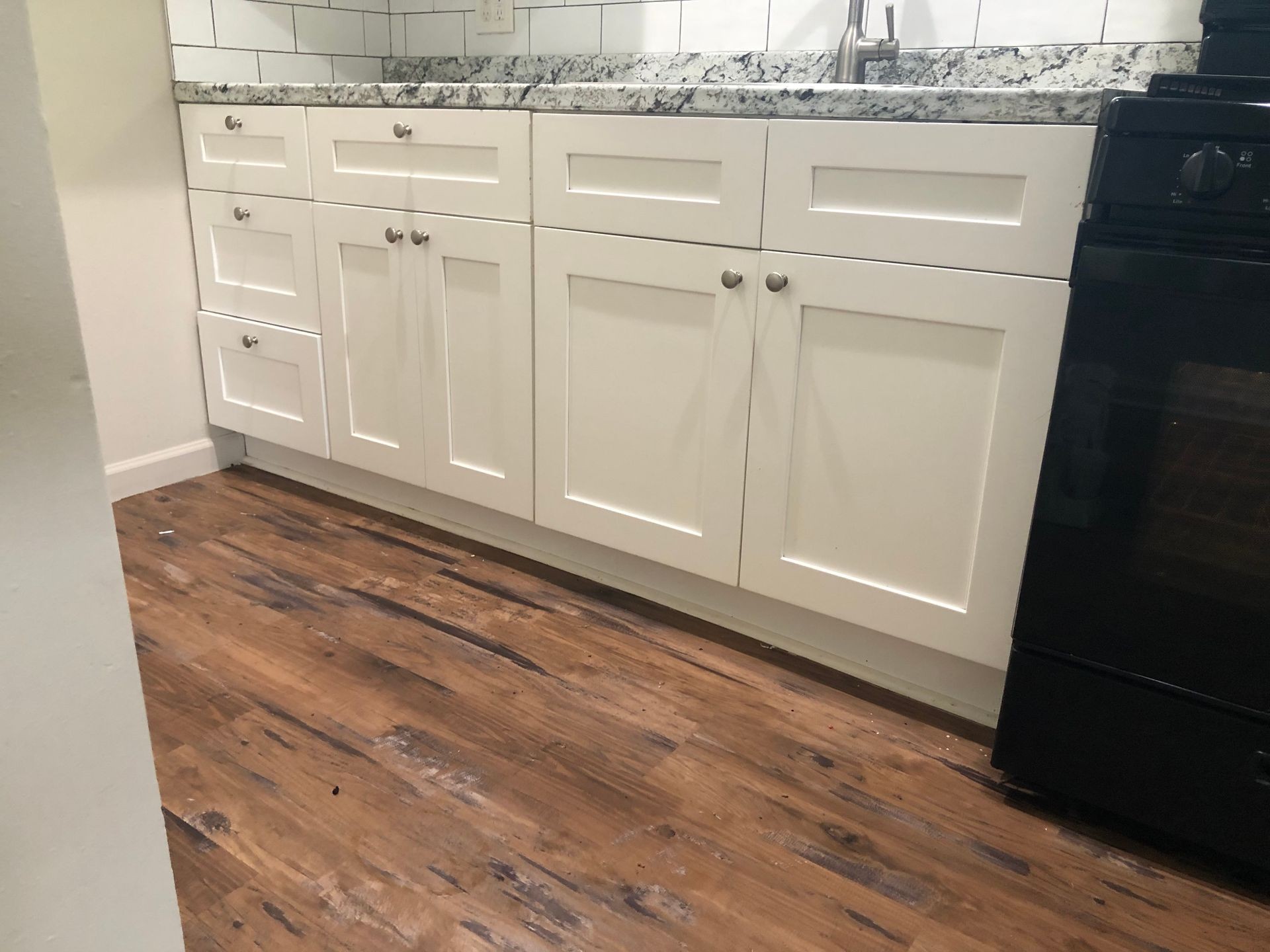 Kitchen cabinets with white doors, a granite countertop, and a wooden floor.